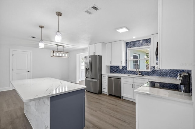 2175 Edythe Dr, Dunedin, FL 34698 - kitchen featuring appliances with stainless steel finishes, a center island, light wood-style flooring, decorative backsplash, and white cabinets