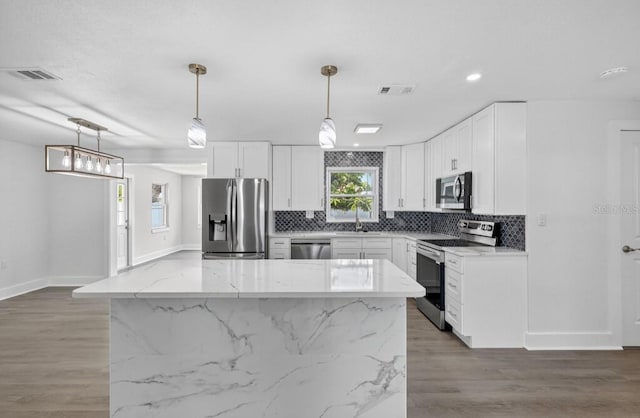 2175 Edythe Dr, Dunedin, FL 34698 - kitchen with stainless steel appliances, decorative backsplash, light stone countertops, light wood-style floors, and white cabinetry