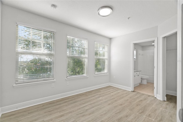 unfurnished bedroom featuring baseboards, light wood-style flooring, and ensuite bath