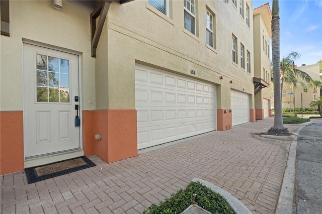 view of exterior entry with an attached garage, stucco siding, and driveway
