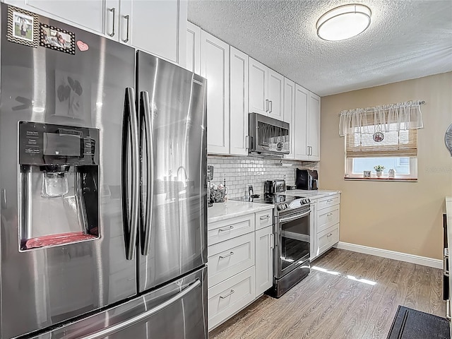 kitchen with appliances with stainless steel finishes, light wood-style flooring, white cabinets, baseboards, and tasteful backsplash