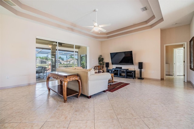 living area with a ceiling fan, a tray ceiling, light tile patterned flooring, and visible vents