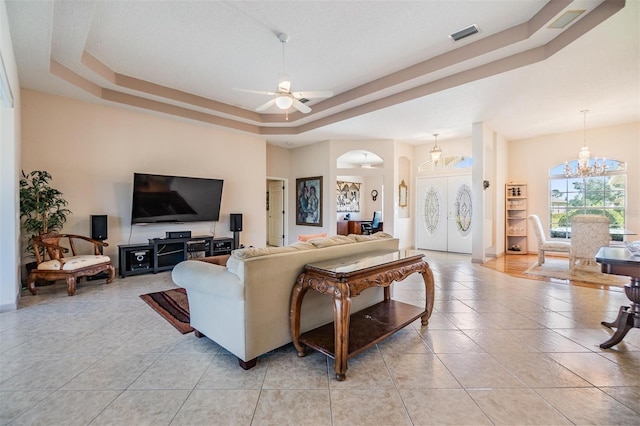 living area featuring arched walkways, ceiling fan with notable chandelier, light tile patterned floors, a tray ceiling, and visible vents