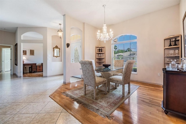 dining space featuring arched walkways, baseboards, an inviting chandelier, and light wood finished floors