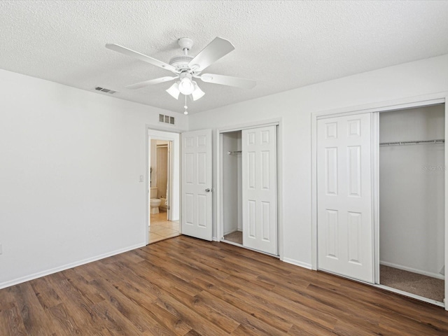 unfurnished bedroom with multiple closets, baseboards, wood finished floors, and visible vents