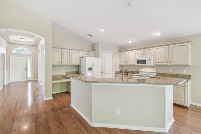 kitchen featuring white appliances, arched walkways, wood finished floors, and a kitchen island with sink