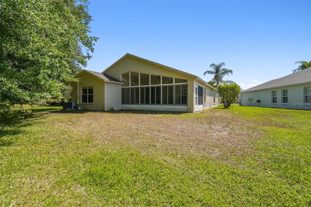 rear view of property with a yard, stucco siding, a sunroom, and central AC
