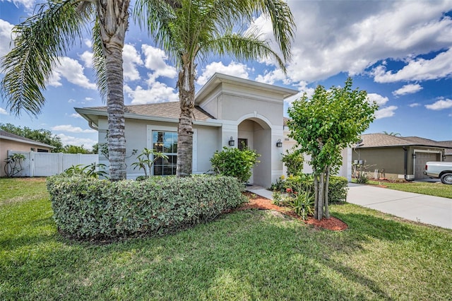mediterranean / spanish-style house with driveway, fence, a front lawn, and stucco siding