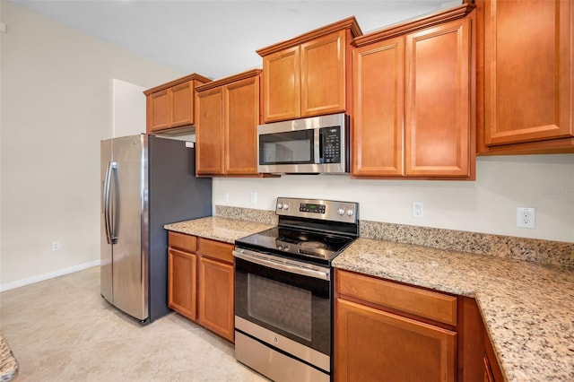 kitchen featuring baseboards, light stone countertops, stainless steel appliances, and brown cabinets