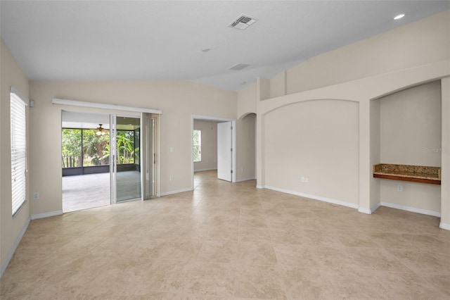 empty room with light tile patterned flooring, vaulted ceiling, a wealth of natural light, and visible vents