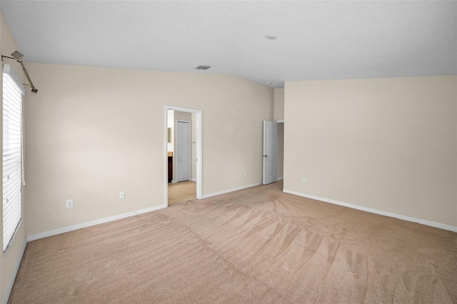 empty room with light colored carpet, baseboards, vaulted ceiling, and visible vents