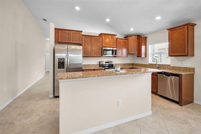 kitchen with a kitchen island, appliances with stainless steel finishes, light stone countertops, brown cabinets, and a sink
