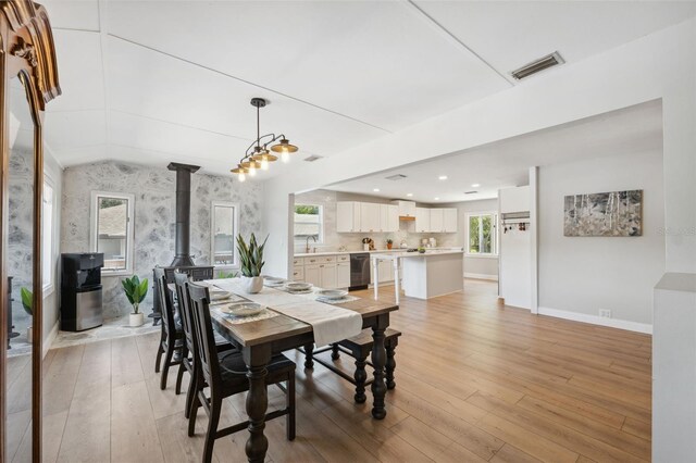 dining room with a wood stove, baseboards, wallpapered walls, light wood-type flooring, and visible vents