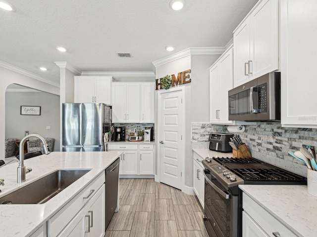 8630 Campus Woods Way, New Port Richey, FL 34655 - kitchen featuring ornamental molding, arched walkways, white cabinets, a sink, and appliances with stainless steel finishes