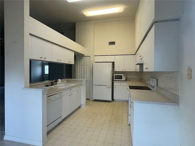 kitchen featuring a sink, white appliances, light floors, visible vents, and a high ceiling