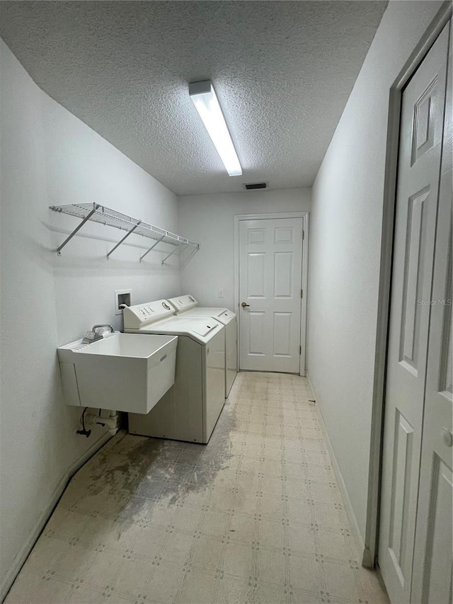 clothes washing area featuring a sink, separate washer and dryer, laundry area, light floors, and a textured ceiling