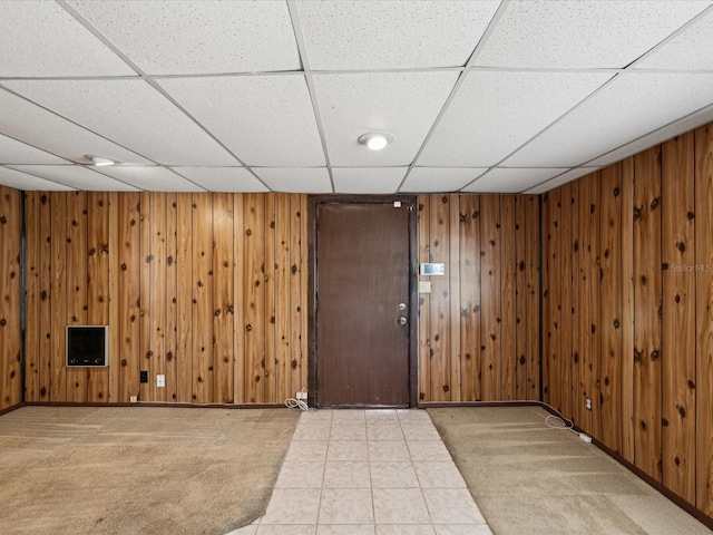 carpeted foyer featuring baseboards, a drop ceiling, and wood walls