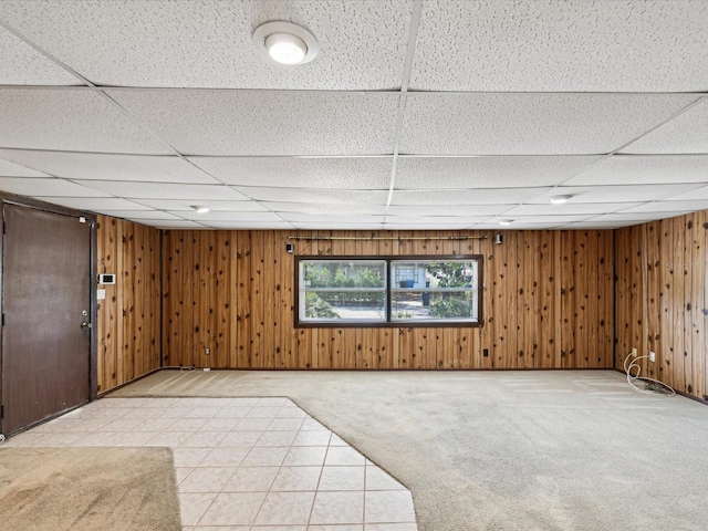basement with light carpet, a drop ceiling, and wood walls