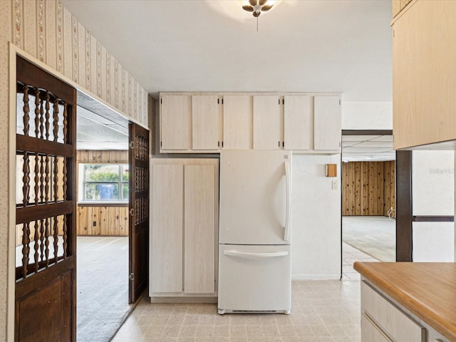 kitchen with wooden walls, cream cabinets, light colored carpet, light countertops, and freestanding refrigerator