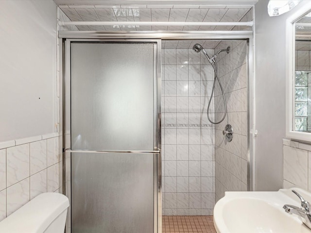 bathroom featuring a sink, a shower stall, toilet, and tile walls