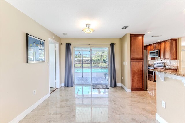 kitchen featuring light stone countertops, appliances with stainless steel finishes, brown cabinetry, baseboards, and visible vents