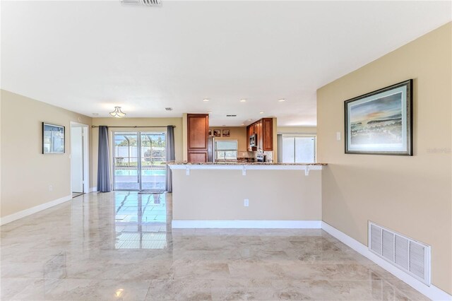 kitchen featuring brown cabinets, a kitchen breakfast bar, stone countertops, stainless steel microwave, and visible vents