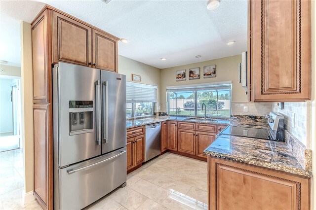 kitchen with dark stone counters, stainless steel appliances, decorative backsplash, and a sink