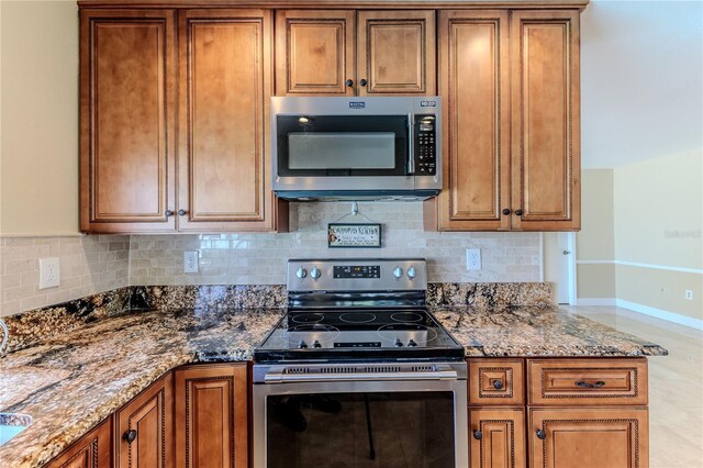 kitchen with stone countertops, baseboards, brown cabinets, backsplash, and stainless steel appliances