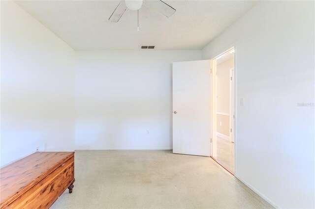 empty room with visible vents, a ceiling fan, and light carpet