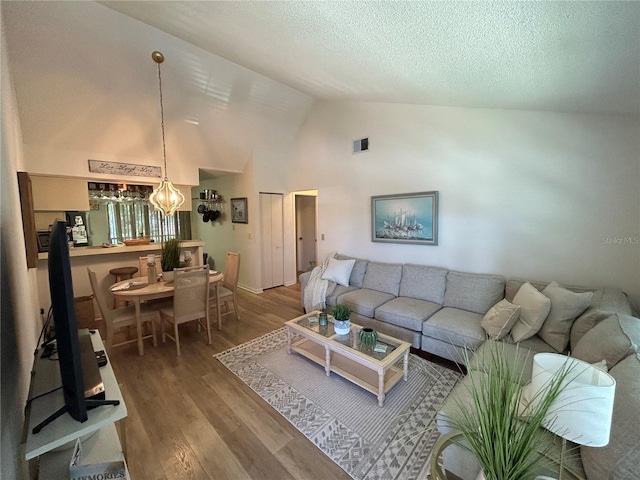 living area with visible vents, wood finished floors, high vaulted ceiling, a textured ceiling, and a chandelier