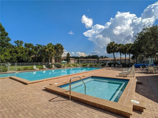 community pool with a hot tub, a patio, and fence