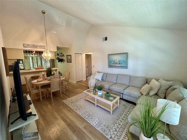 living area with an inviting chandelier, a textured ceiling, high vaulted ceiling, wood finished floors, and visible vents