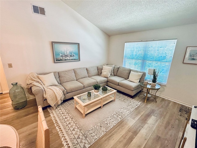 living area featuring visible vents, lofted ceiling, wood finished floors, baseboards, and a textured ceiling