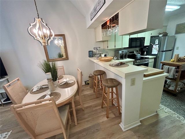 kitchen with an inviting chandelier, stainless steel appliances, a peninsula, wood finished floors, and lofted ceiling