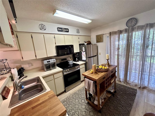 kitchen featuring a textured ceiling, a sink, light countertops, light wood-style floors, and stainless steel appliances