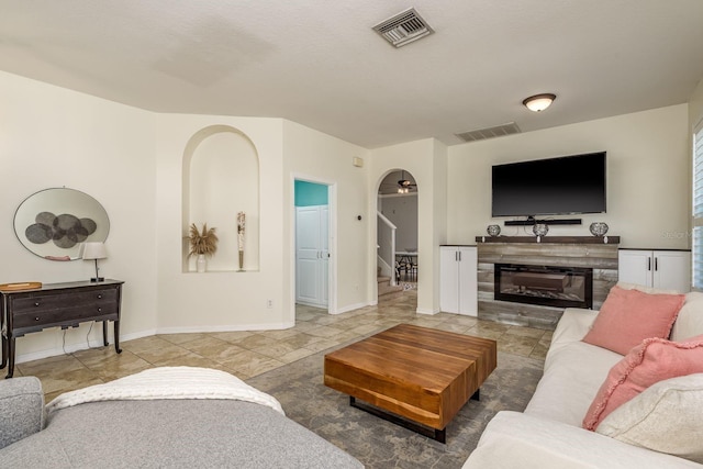 tiled living room featuring a glass covered fireplace, ceiling fan, stairs, and visible vents
