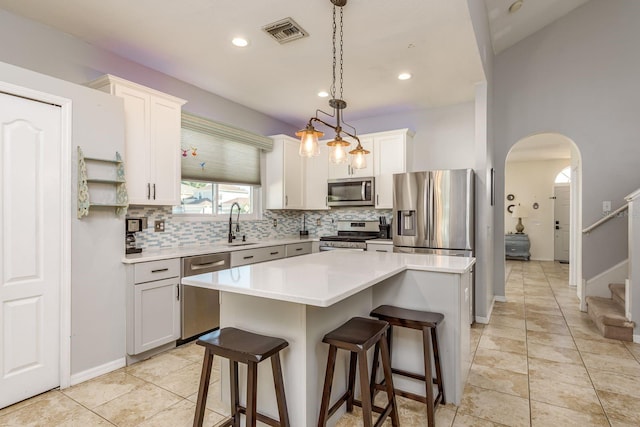 kitchen with appliances with stainless steel finishes, a kitchen breakfast bar, arched walkways, backsplash, and visible vents