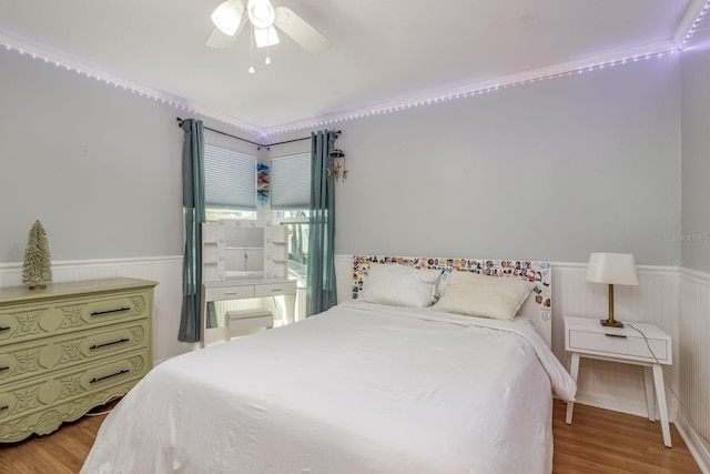 bedroom with a wainscoted wall, a ceiling fan, and wood finished floors