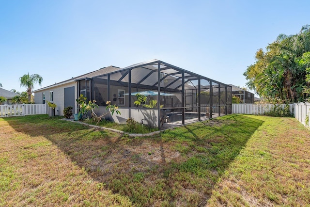 rear view of house with a lawn, a fenced backyard, and glass enclosure