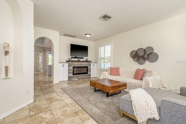 living room featuring visible vents, arched walkways, baseboards, and a glass covered fireplace