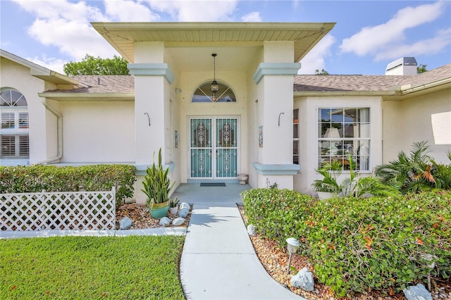 entrance to property featuring a shingled roof and stucco siding