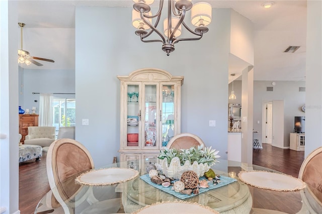 dining space featuring visible vents, ceiling fan with notable chandelier, a towering ceiling, and wood finished floors