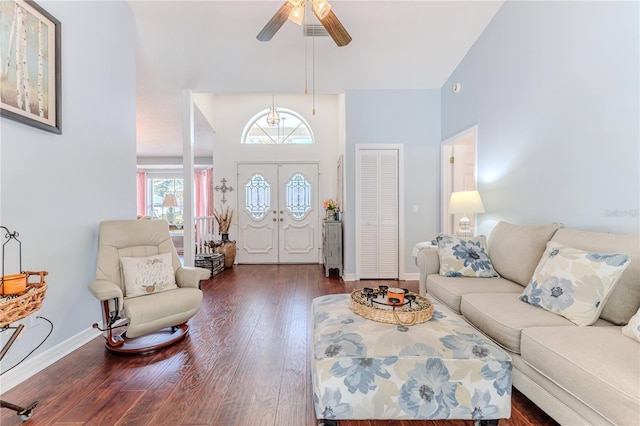 living room with a ceiling fan, dark wood-style flooring, visible vents, baseboards, and a high ceiling
