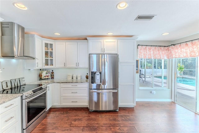 kitchen featuring wall chimney range hood, dark wood-style flooring, glass insert cabinets, stainless steel appliances, and white cabinetry