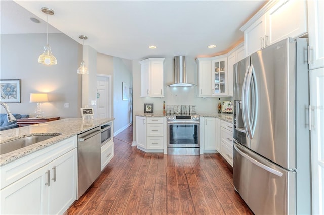 kitchen with wall chimney range hood, appliances with stainless steel finishes, a sink, white cabinetry, and glass insert cabinets