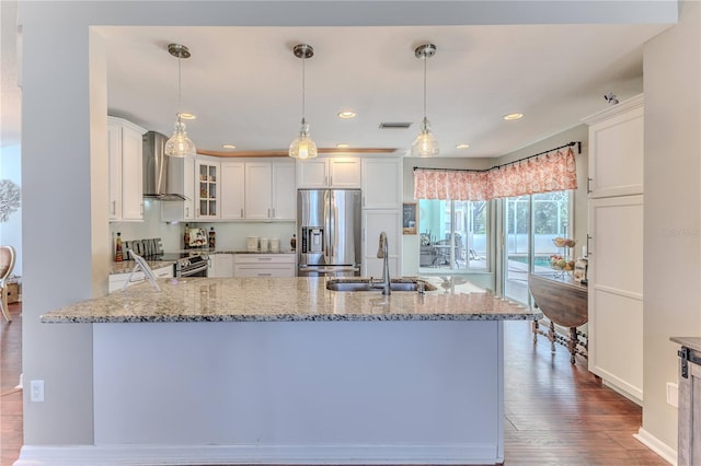 kitchen with wall chimney range hood, stainless steel appliances, light stone countertops, and a sink