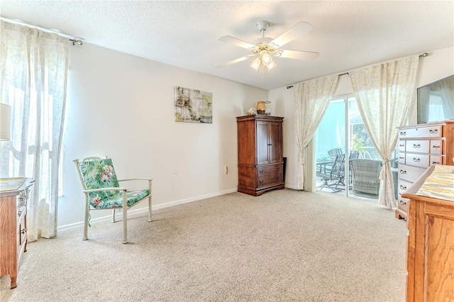 living area with baseboards, ceiling fan, carpet, and a textured ceiling