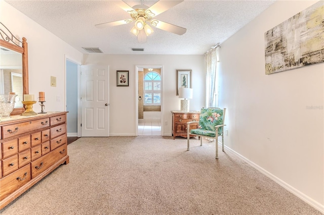 sitting room featuring light colored carpet, ceiling fan, visible vents, and a textured ceiling