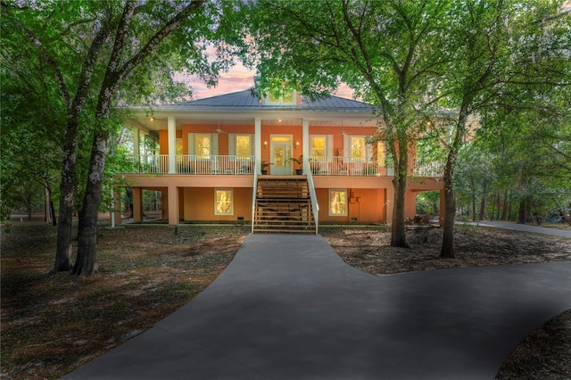 raised beach house featuring covered porch, stucco siding, a standing seam roof, metal roof, and stairway