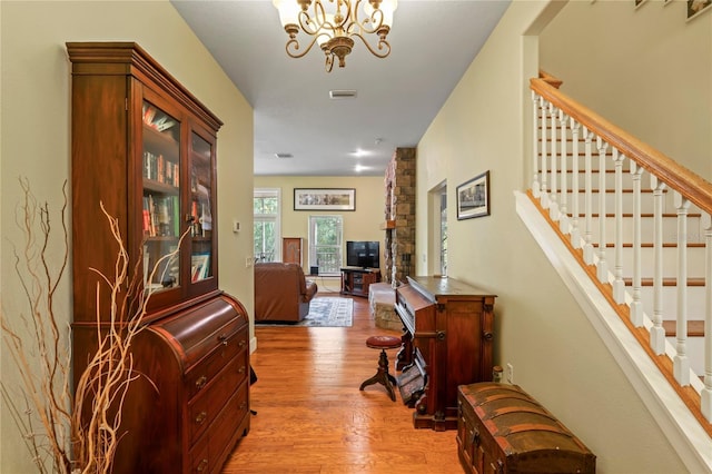 hallway with an inviting chandelier, stairway, light wood-type flooring, and visible vents